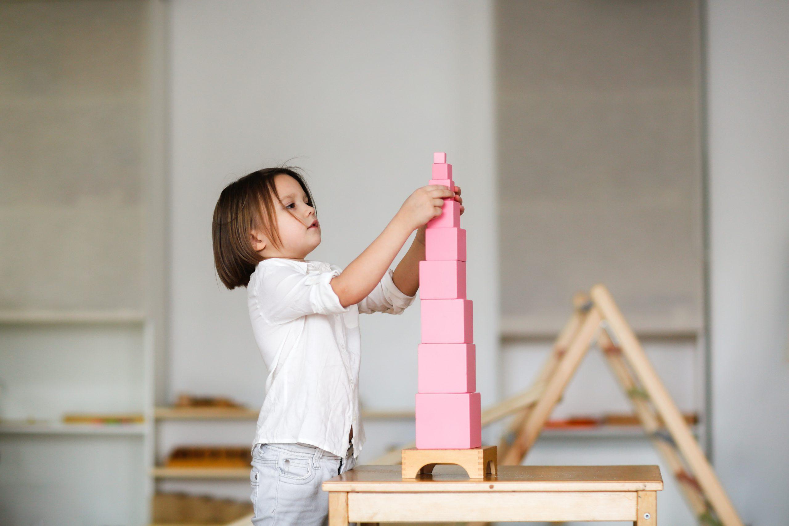 child girl playing with pink tower, developing sensory activitie